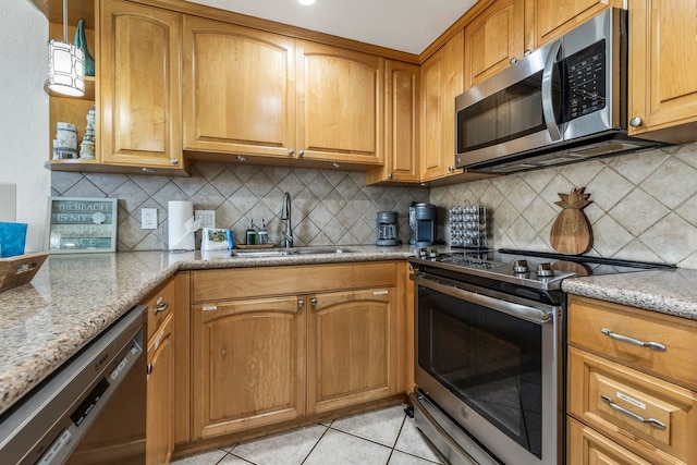 kitchen with sink, light tile patterned floors, light stone countertops, and appliances with stainless steel finishes