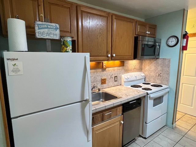 kitchen with backsplash, appliances with stainless steel finishes, tile countertops, light tile patterned flooring, and sink