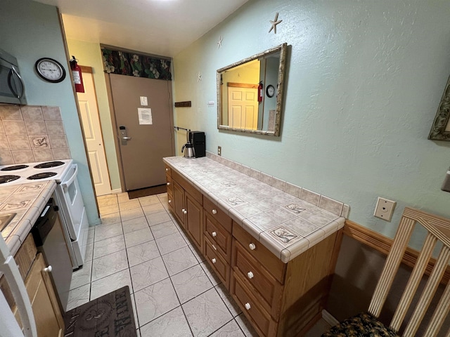 715 S Kihei Rd Unit D144, Kihei, HI 96753 - kitchen with tile countertops, brown cabinetry, white range with electric stovetop, tasteful backsplash, and light marble finish floors