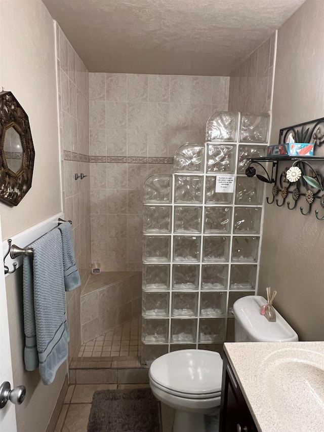 bathroom with a textured ceiling, toilet, tiled shower, vanity, and tile patterned flooring