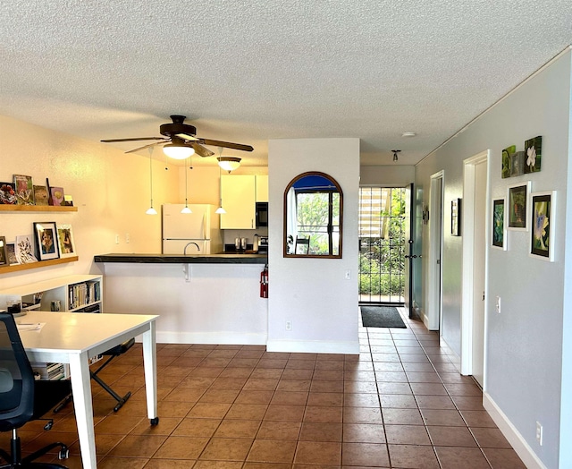 kitchen with white refrigerator, ceiling fan, dark tile patterned floors, a kitchen bar, and kitchen peninsula