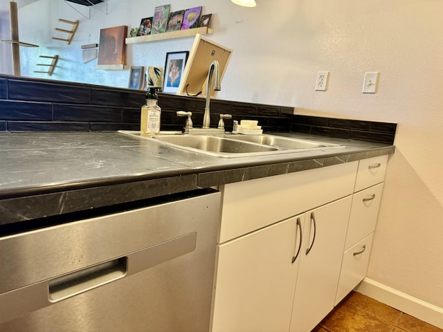 kitchen featuring sink, stainless steel dishwasher, dark tile patterned floors, stainless steel counters, and white cabinetry