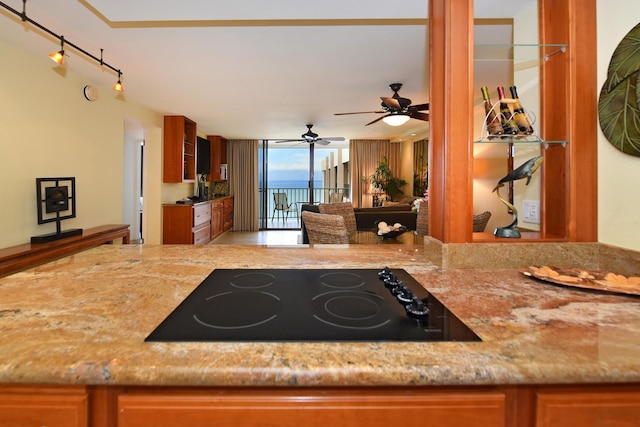 4327 Lower Honoapiilani Rd Unit 1203, Lahaina, HI 96761 - kitchen featuring black electric cooktop, ceiling fan, light stone counters, and brown cabinets