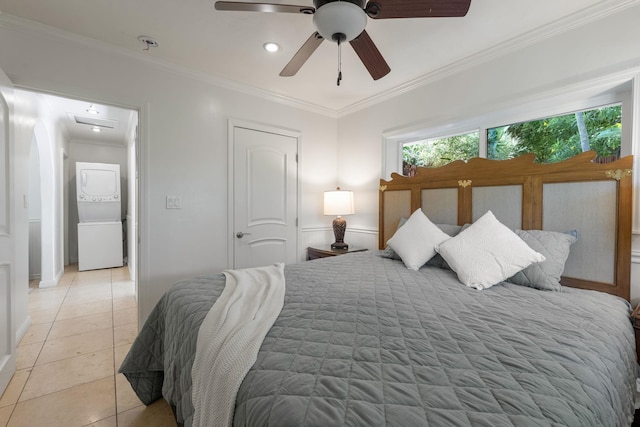 bedroom featuring ceiling fan, crown molding, light tile patterned floors, and stacked washer and dryer