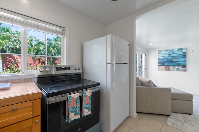 kitchen featuring tile countertops, stainless steel electric range, light tile patterned floors, a wealth of natural light, and white fridge