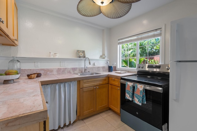 kitchen featuring stainless steel range with electric stovetop, white refrigerator, sink, light tile patterned floors, and tile counters