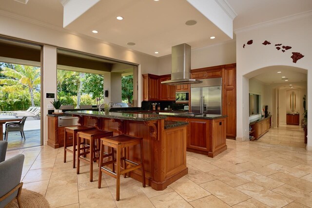 kitchen featuring built in refrigerator, a kitchen island, arched walkways, brown cabinetry, and island range hood