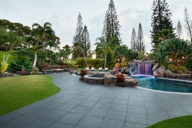 outdoor pool with a patio area, a lawn, and an in ground hot tub