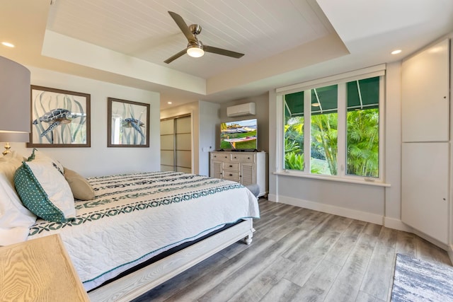 bedroom with hardwood / wood-style floors, ceiling fan, a raised ceiling, and a wall mounted air conditioner