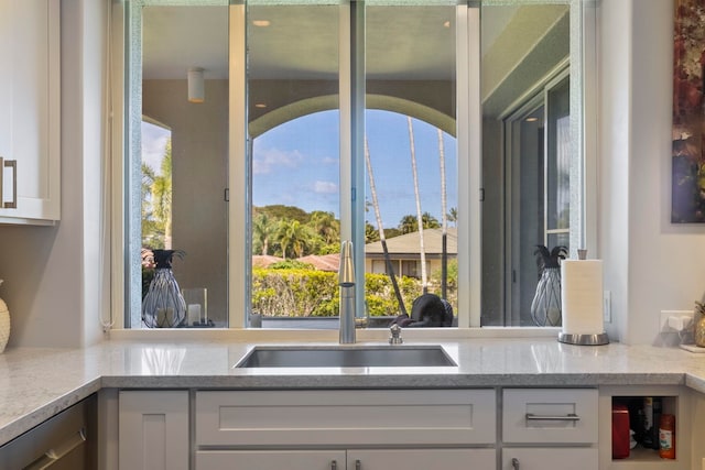 kitchen featuring a healthy amount of sunlight, white cabinetry, sink, and light stone countertops