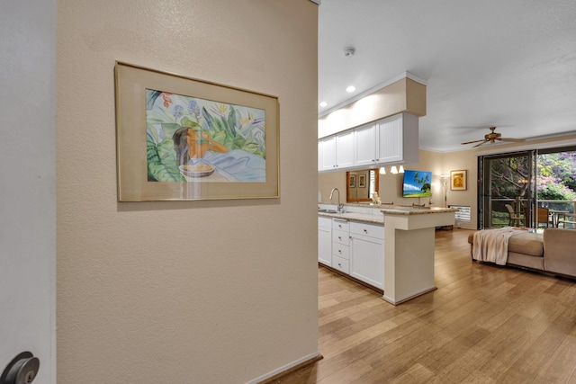 kitchen featuring light stone counters, light wood finished floors, a ceiling fan, open floor plan, and white cabinetry