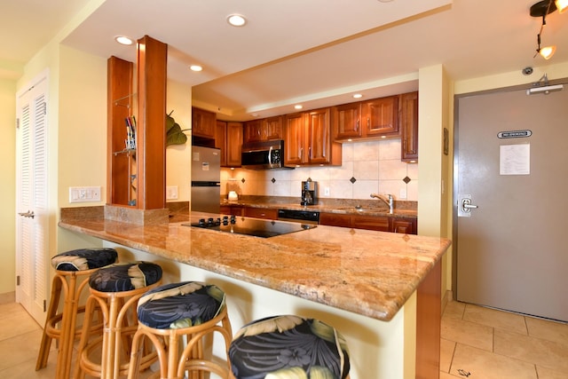 kitchen with appliances with stainless steel finishes, light tile floors, backsplash, a breakfast bar area, and kitchen peninsula