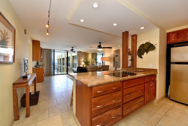 kitchen featuring ceiling fan, stainless steel refrigerator, expansive windows, black electric stovetop, and light stone countertops