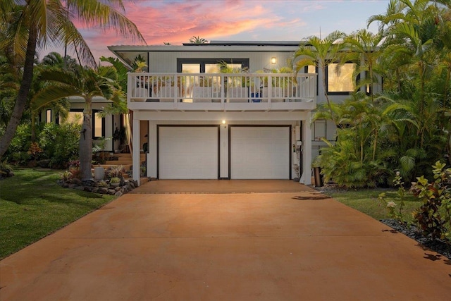 view of front facade featuring driveway, an attached garage, a yard, and a balcony