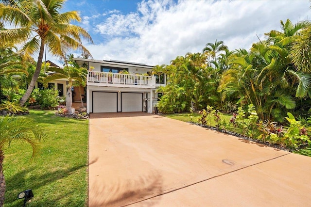 coastal inspired home featuring a garage, driveway, a front yard, solar panels, and a balcony