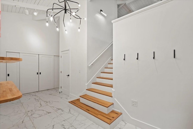 staircase featuring marble finish floors, a chandelier, and a high ceiling