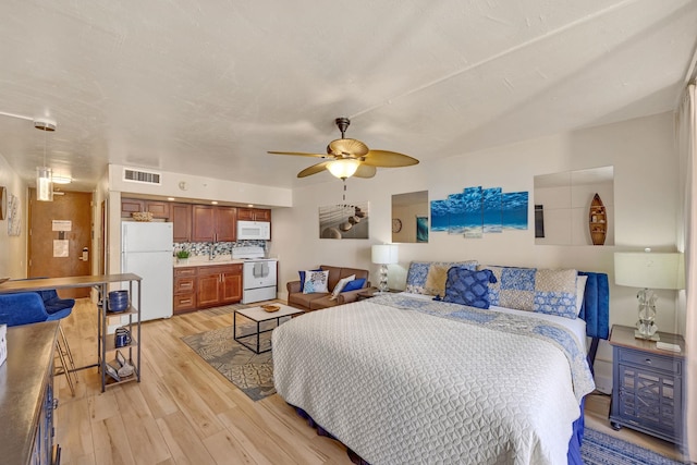 bedroom featuring light wood finished floors, visible vents, freestanding refrigerator, and a ceiling fan