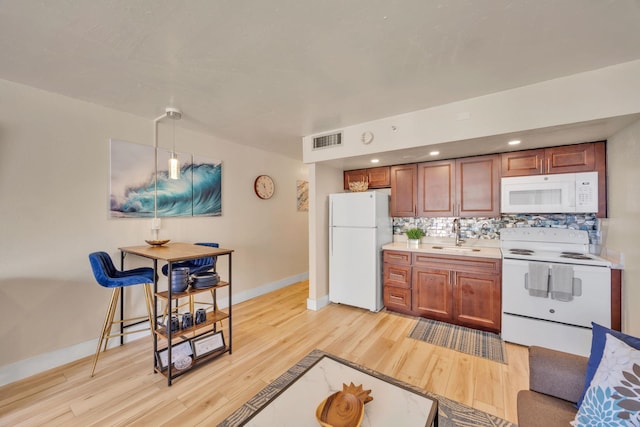 kitchen with visible vents, brown cabinets, a sink, backsplash, and white appliances