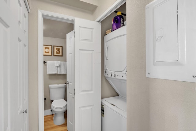 laundry area with electric panel, light wood-style floors, stacked washer and dryer, and laundry area