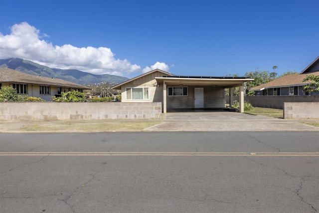 view of front facade with fence, concrete driveway, an attached carport, a mountain view, and concrete block siding