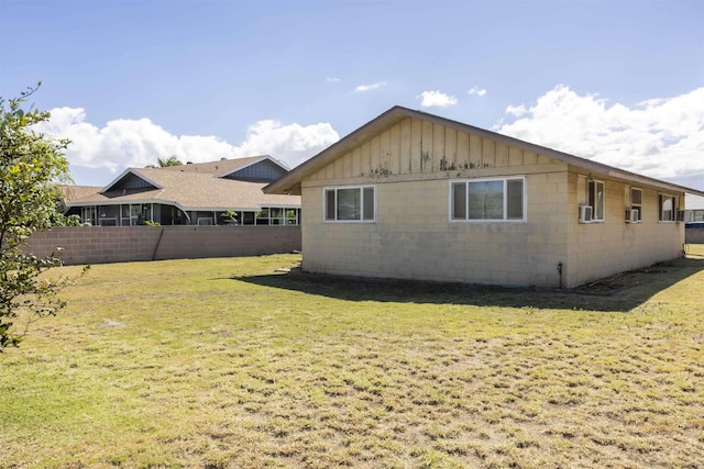 exterior space with concrete block siding, fence, and a lawn