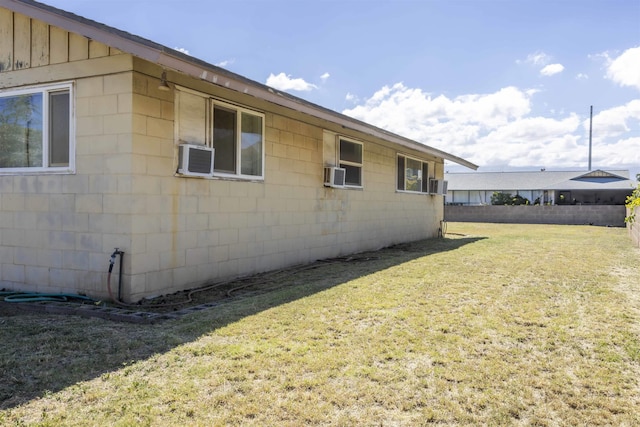 view of side of property with concrete block siding, fence, and a lawn