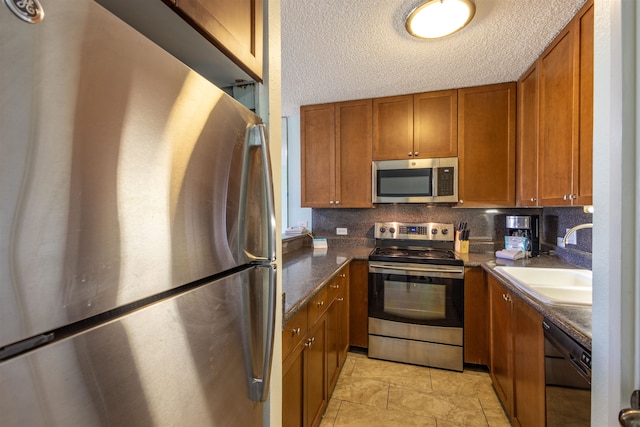 kitchen featuring sink, dark stone countertops, a textured ceiling, decorative backsplash, and appliances with stainless steel finishes