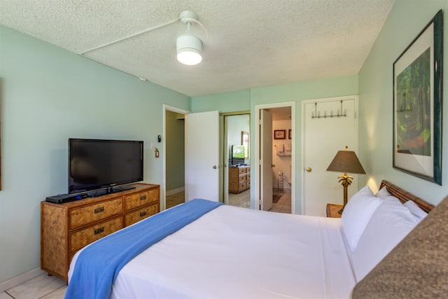 tiled bedroom with ensuite bath, ceiling fan, and a textured ceiling