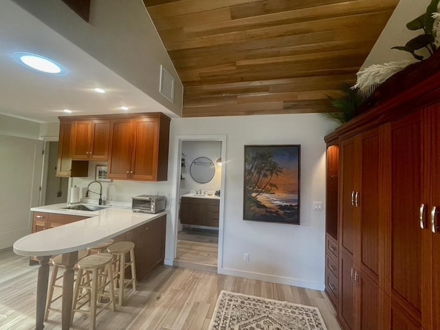 kitchen with light wood finished floors, a breakfast bar area, brown cabinets, light countertops, and a sink