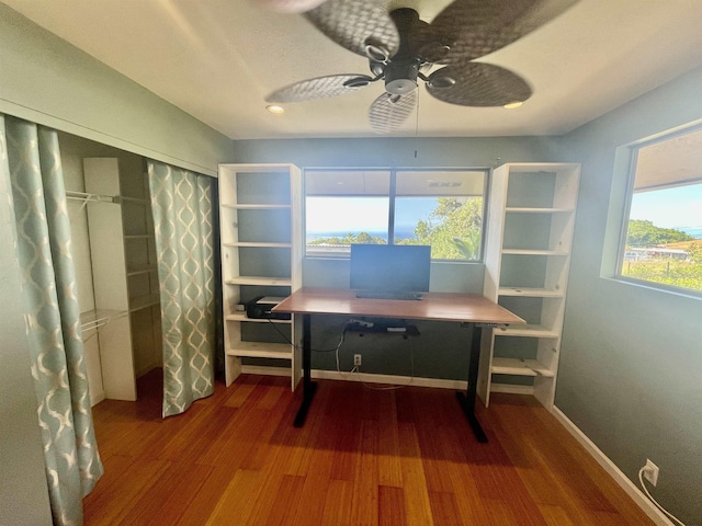 unfurnished office featuring dark wood-type flooring, a ceiling fan, and baseboards