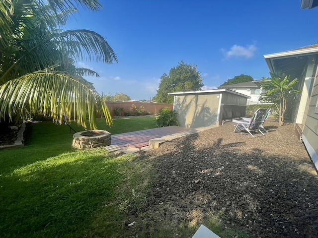 view of yard featuring a deck, an outbuilding, a fire pit, fence, and a storage unit