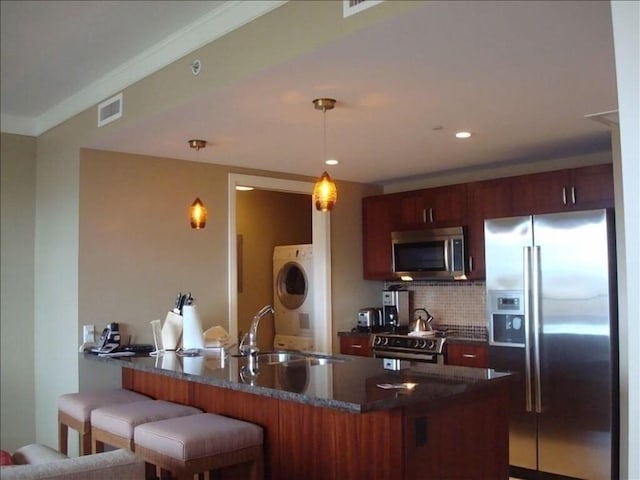 kitchen featuring kitchen peninsula, stainless steel appliances, sink, decorative light fixtures, and stacked washer / dryer