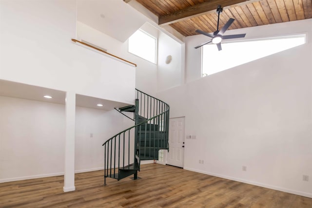 staircase with a towering ceiling, beamed ceiling, hardwood / wood-style flooring, ceiling fan, and wooden ceiling