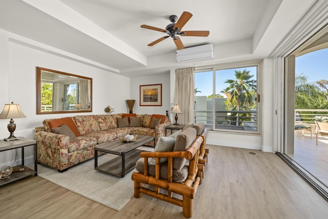 living room featuring a wall mounted air conditioner, light hardwood / wood-style floors, a raised ceiling, and ceiling fan