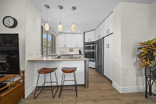 kitchen featuring pendant lighting, white cabinetry, hardwood / wood-style floors, stainless steel appliances, and kitchen peninsula