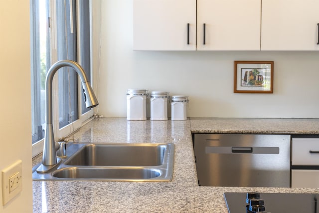 interior details with light stone counters, sink, stainless steel dishwasher, and white cabinets