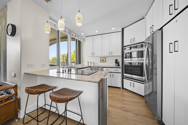 kitchen with decorative light fixtures, appliances with stainless steel finishes, kitchen peninsula, light stone countertops, and white cabinets