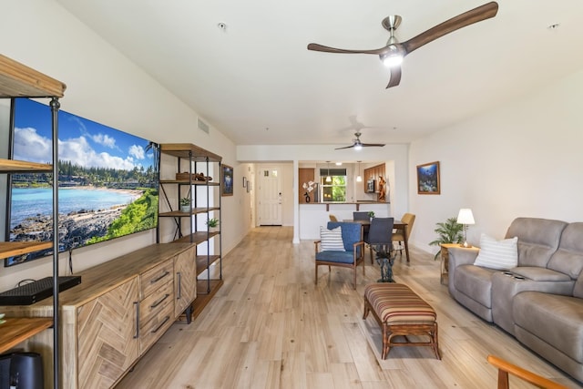living room featuring light wood finished floors, a ceiling fan, visible vents, and baseboards