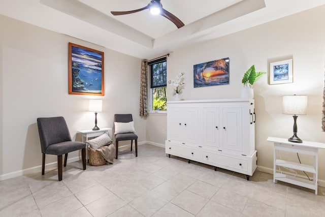 living area with baseboards, a ceiling fan, light tile patterned flooring, and a tray ceiling