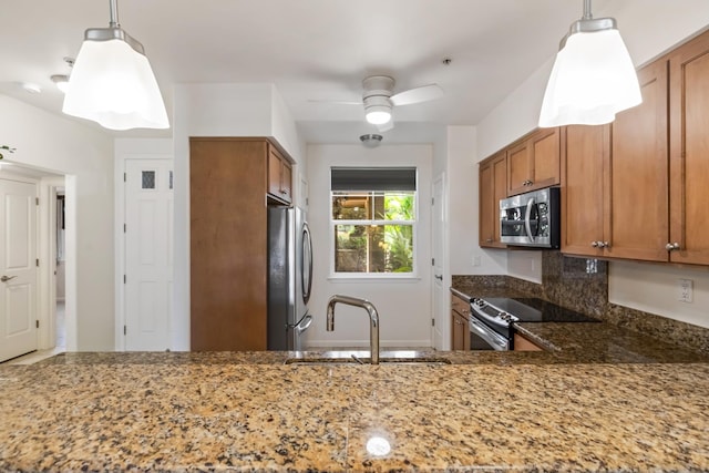 kitchen featuring light stone countertops, stainless steel appliances, brown cabinets, ceiling fan, and a sink