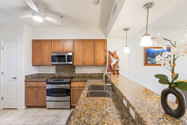 kitchen with dark stone counters, a sink, brown cabinets, and stainless steel appliances