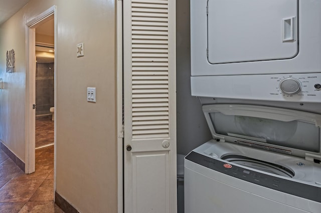 laundry area with dark tile patterned floors, stacked washing maching and dryer, and laundry area