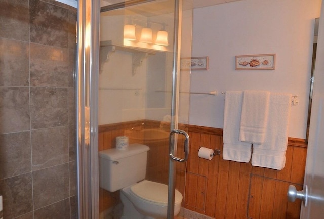 bathroom featuring toilet, a shower with shower door, and wooden walls