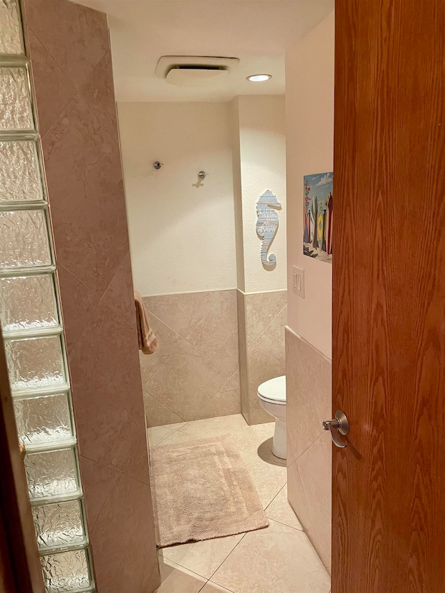 bathroom with toilet, tile patterned flooring, and tile walls