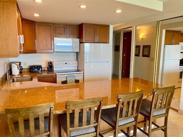 kitchen with stone countertops, light tile patterned floors, sink, a breakfast bar area, and white appliances