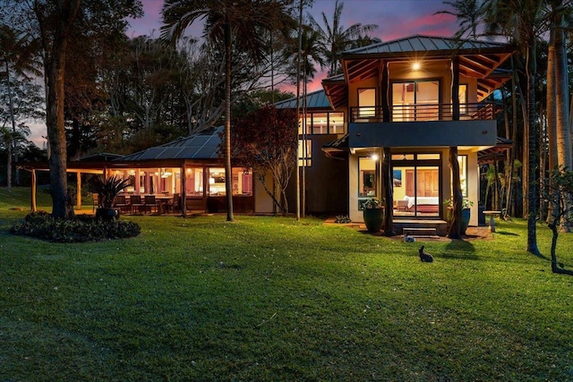 back house at dusk featuring a balcony and a lawn