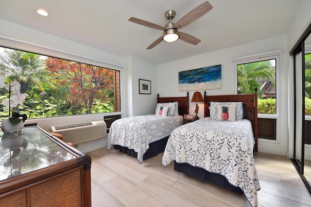 bedroom with ceiling fan, an AC wall unit, and light hardwood / wood-style flooring