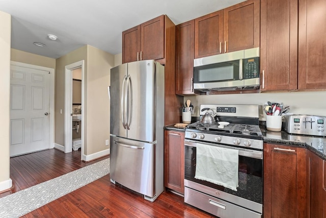 kitchen featuring appliances with stainless steel finishes, dark hardwood / wood-style floors, and dark stone counters