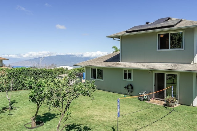 back of property featuring a mountain view, a yard, and solar panels