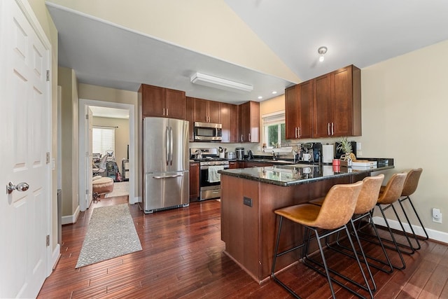 kitchen with vaulted ceiling, appliances with stainless steel finishes, dark wood-type flooring, kitchen peninsula, and a breakfast bar